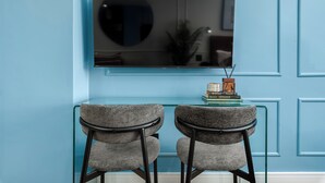 A modern room with a blue wall, a glass table with two chairs, and a flat-screen TV mounted above. - Modern Studio in The Valour | De Waterkant Luxury (Cape Town)
