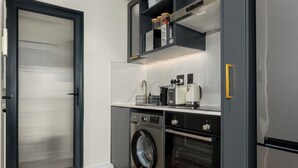 A compact kitchen with a washing machine, oven, and a coffee maker on the countertop. - Modern Studio in The Valour | De Waterkant Luxury (Cape Town)