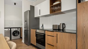 A compact kitchen with a built-in washer, a stainless steel refrigerator, and wooden cabinetry.
