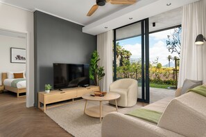 Een moderne woonkamer met een flatscreen televisie, een houten salontafel, een beige bank en een grote schuifdeur naar een balkon met uitzicht op groen en bergen.