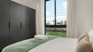 A modern hotel room with a large bed, a green throw blanket, and a view of the outdoors.