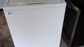 En vaskemaskine og tørretumbler fra Whirlpool med kontrolpanel, et klistermærke og en sort komfur i baggrunden.