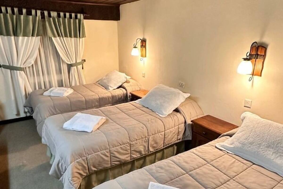 Een hotelkamer met drie bedden, elk voorzien van een witte handdoek, houten hoofdeinden en wandlampen.