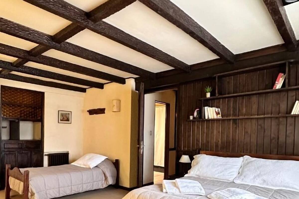 Een knus slaapkamer met een groot bed, een houten bankje en een klein tafeltje.