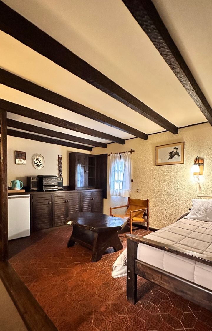 Una habitación acogedora con cama, un banco de madera, una mesita y una kitchenette.