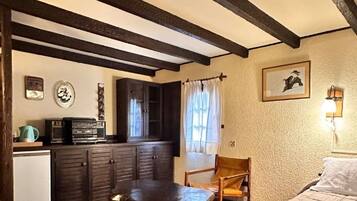 Una habitación acogedora con cama, un banco de madera, una mesita y una kitchenette.