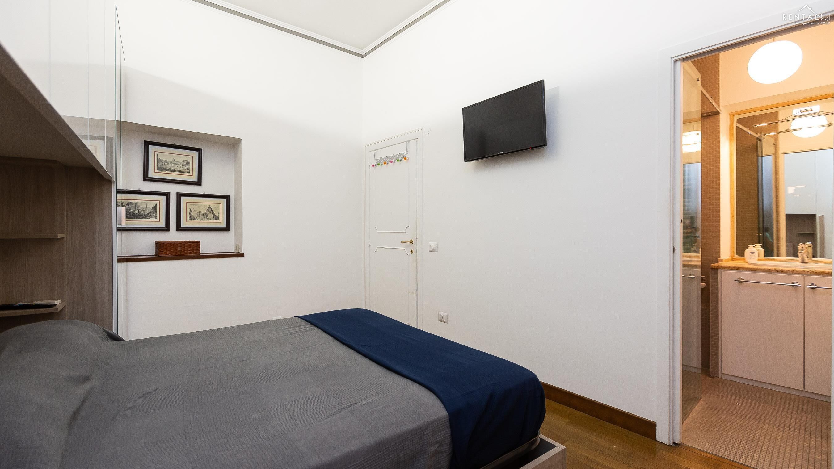 A bedroom with a bed, a TV mounted on the wall, and a door leading to a bathroom.