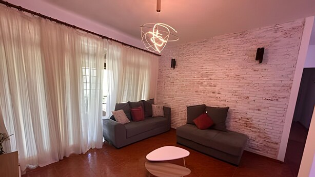 A modern living room with two sofas, a coffee table, and a brick wall. - Casa Refúgio Verde Conforto em SJBVista (São João da Boa Vista)