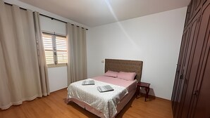 A bedroom with a bed, a nightstand, a window with blinds, and a wardrobe. - Casa Refúgio Verde Conforto em SJBVista (São João da Boa Vista)