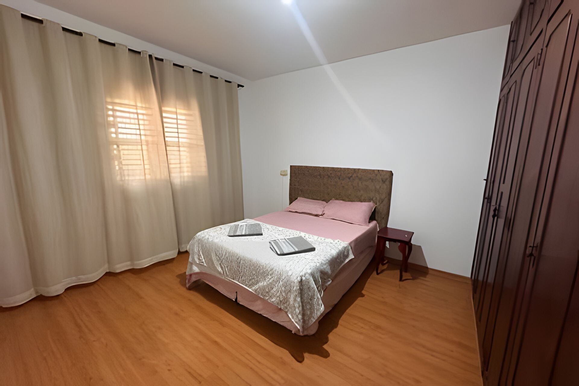 A bedroom with a bed, a nightstand, a wardrobe, and a window with curtains.