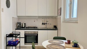 A compact kitchen with white cabinets, a stove, a sink, and a small dining area with a table and chairs.