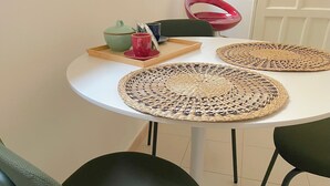 A round table with two woven placemats, a green teapot, a red cup, and a smartphone on a tray.