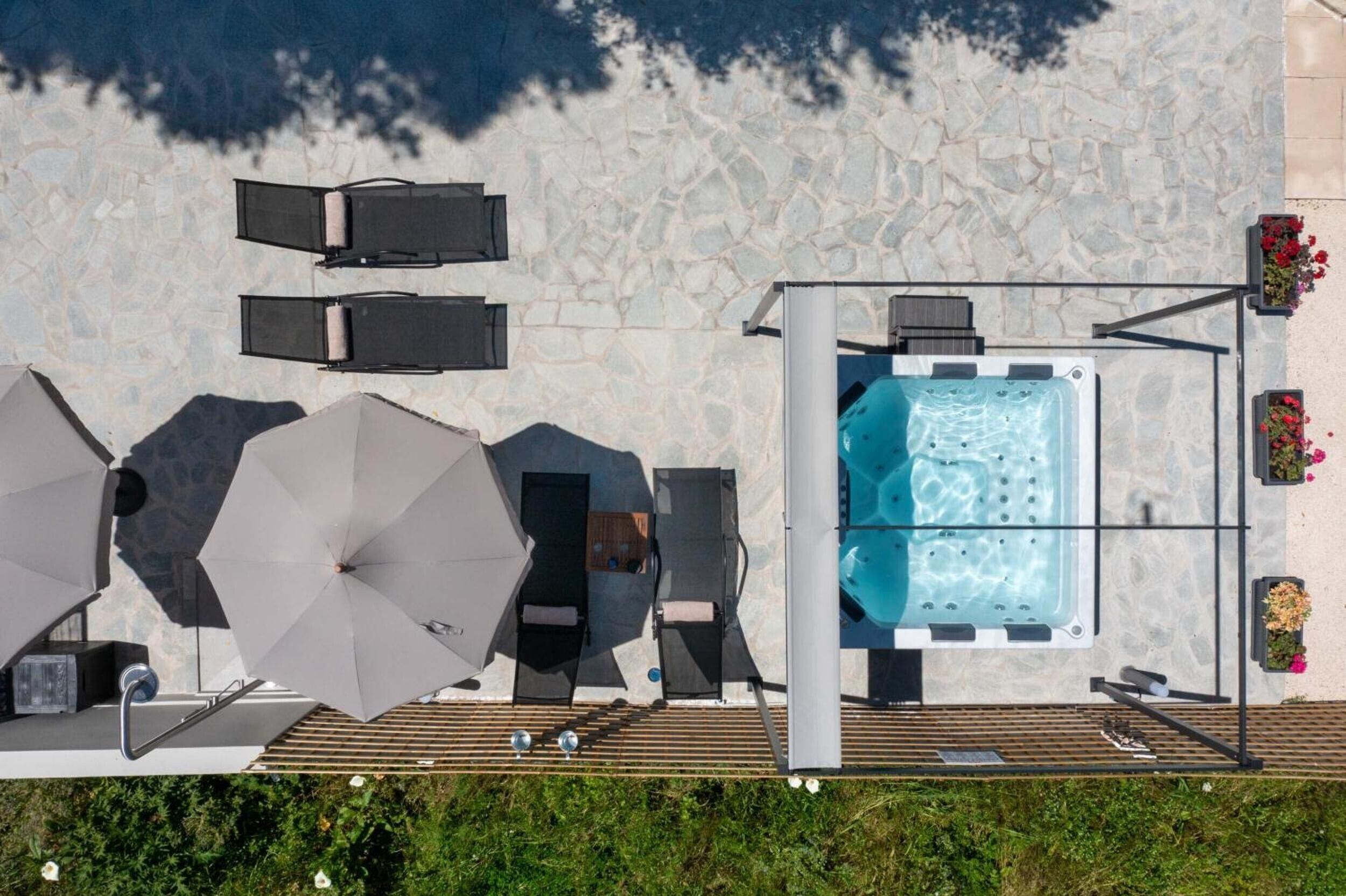 A rooftop pool area with lounge chairs, umbrellas, and a hot tub.