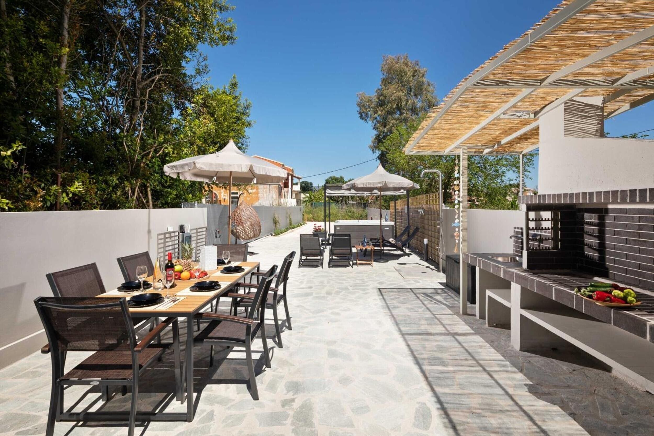 An outdoor patio with a dining table, chairs, umbrellas, and a barbecue grill.
