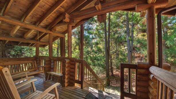 A wooden deck with benches and a staircase leading to a forested area.