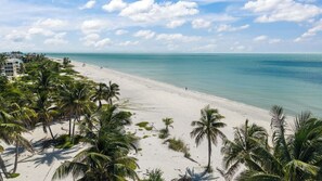 A beach with white sand, palm trees, and a clear blue sea.