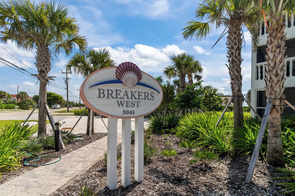 A sign for "BREAKERS WEST" with a shell logo, surrounded by palm trees and a building in the background.