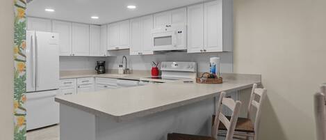 A modern kitchen with white cabinets, a central island, and a microwave.