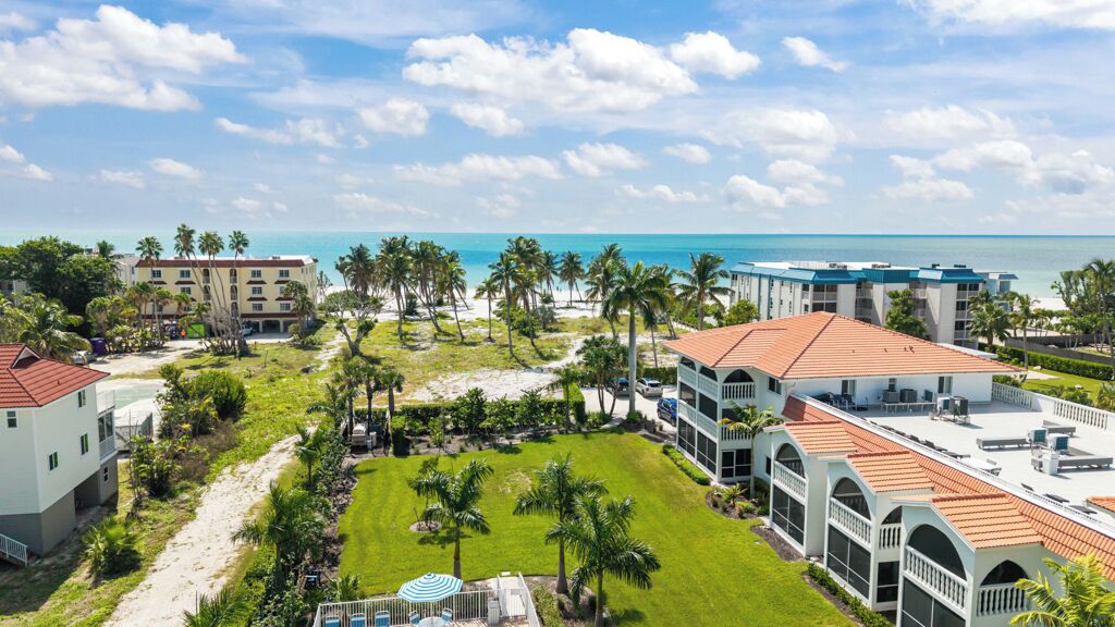 Un resort con varias edificaciones, un patio central con palmeras y vista al océano.