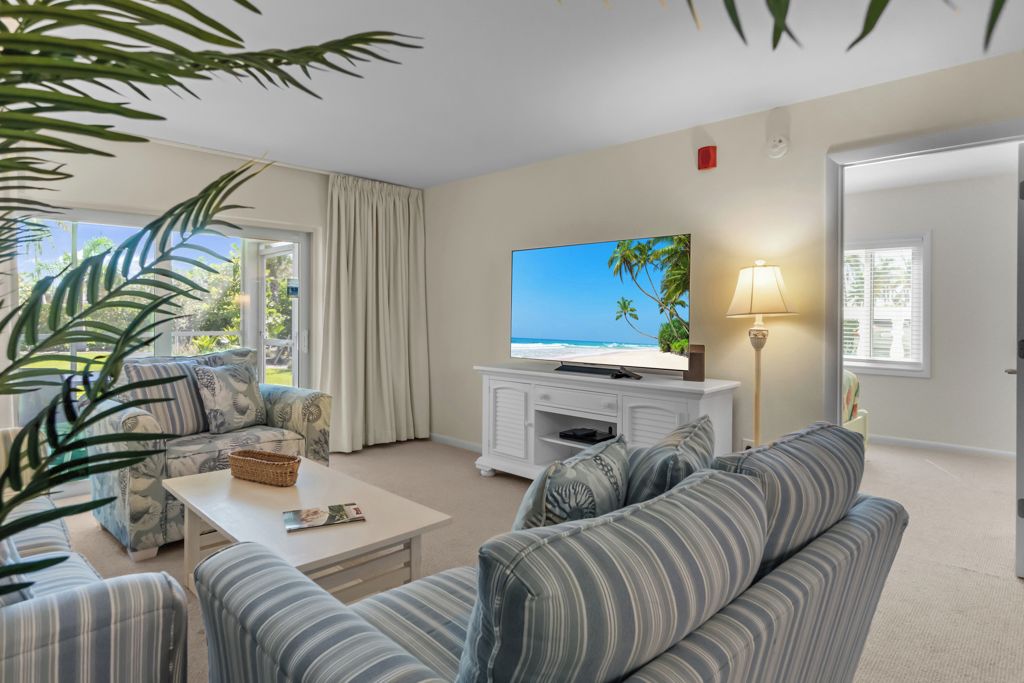 A living room with a large flat-screen TV, a sofa, a coffee table, and a lamp.