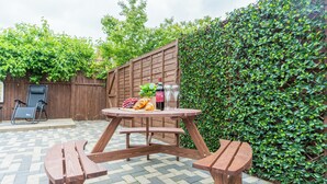 Ein Holztisch mit Bänken, eine Weinflasche und ein Glas Wasser auf einer Terrasse mit Schachbrettfliesen.