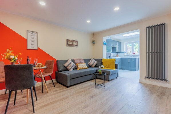 Un salon moderne avec un canapé gris, un mur orange et une petite table sur laquelle est posé un vase.