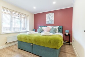Une chambre à coucher avec un lit, une fenêtre avec des stores, un radiateur, une table de chevet avec une lampe et un tableau accroché au mur.