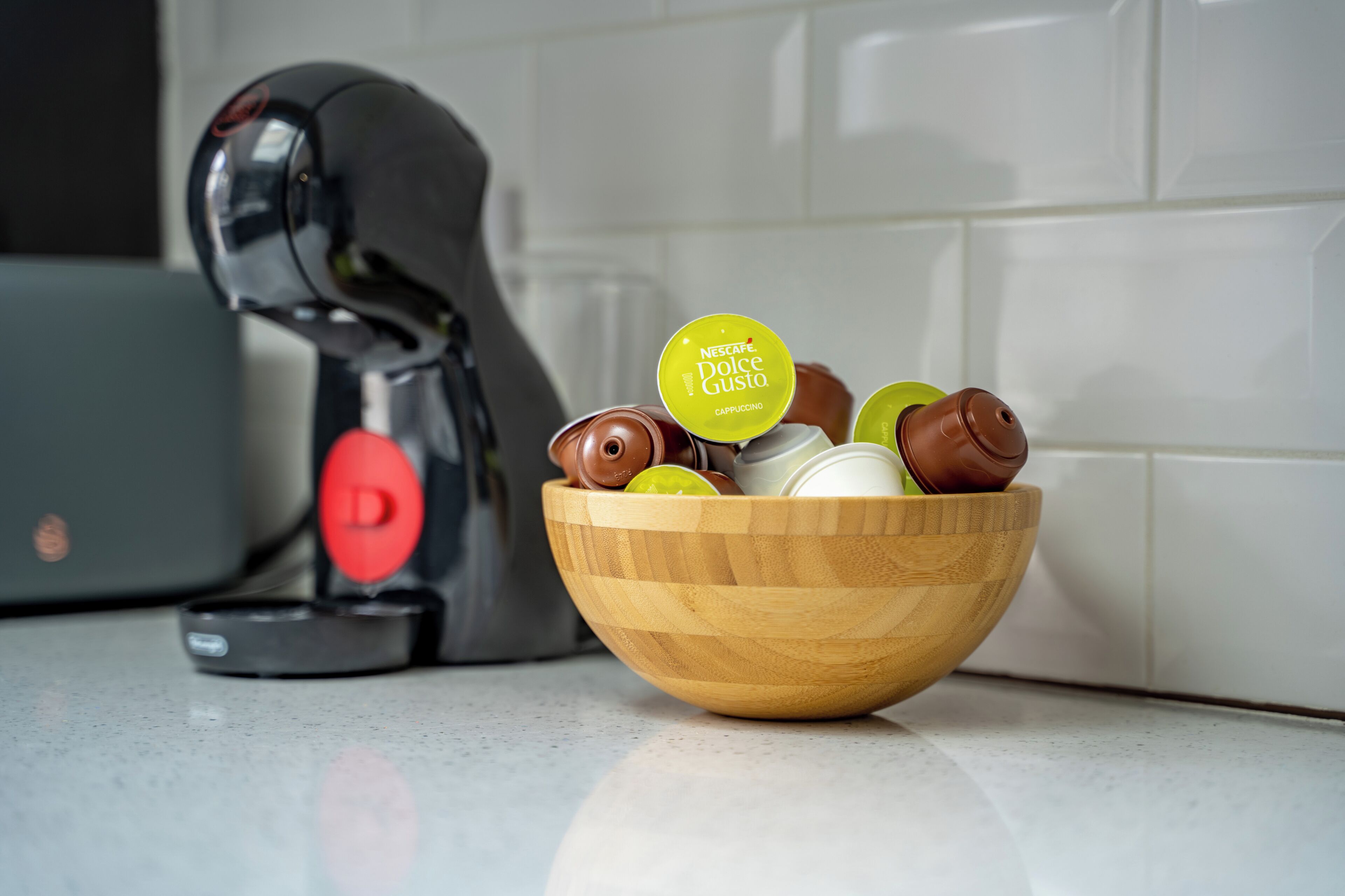 A coffee machine and a wooden bowl with coffee capsules on a countertop.