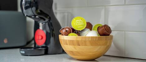 A coffee machine and a wooden bowl with coffee capsules on a countertop.