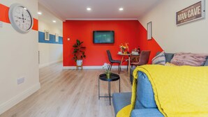Ein modernes Wohnzimmer mit roter Akzentwand, einem Essbereich mit Tisch und Stühlen sowie einem Sofa mit gelber Tagesdecke.