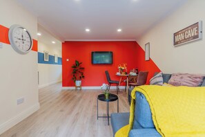 Un salon moderne avec un mur d’accent rouge, un coin repas avec une table et des chaises, et un canapé agrémenté d’un plaid jaune.