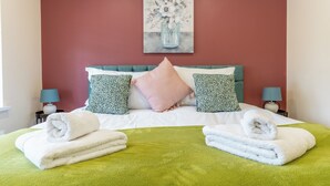 Ein ordentlich gemachtes Bett mit grün-weißer Bettwäsche, zwei Kissen und zwei zusammengerollten Handtüchern.