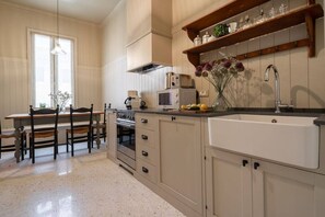 Una cocina equipada con estufa, microondas y lavabo. Hay una mesa de comedor con sillas y una ventana con cortinas.