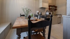 Un coin repas avec une table et des chaises en bois, un vase rempli de fleurs et, au fond, une cuisine.