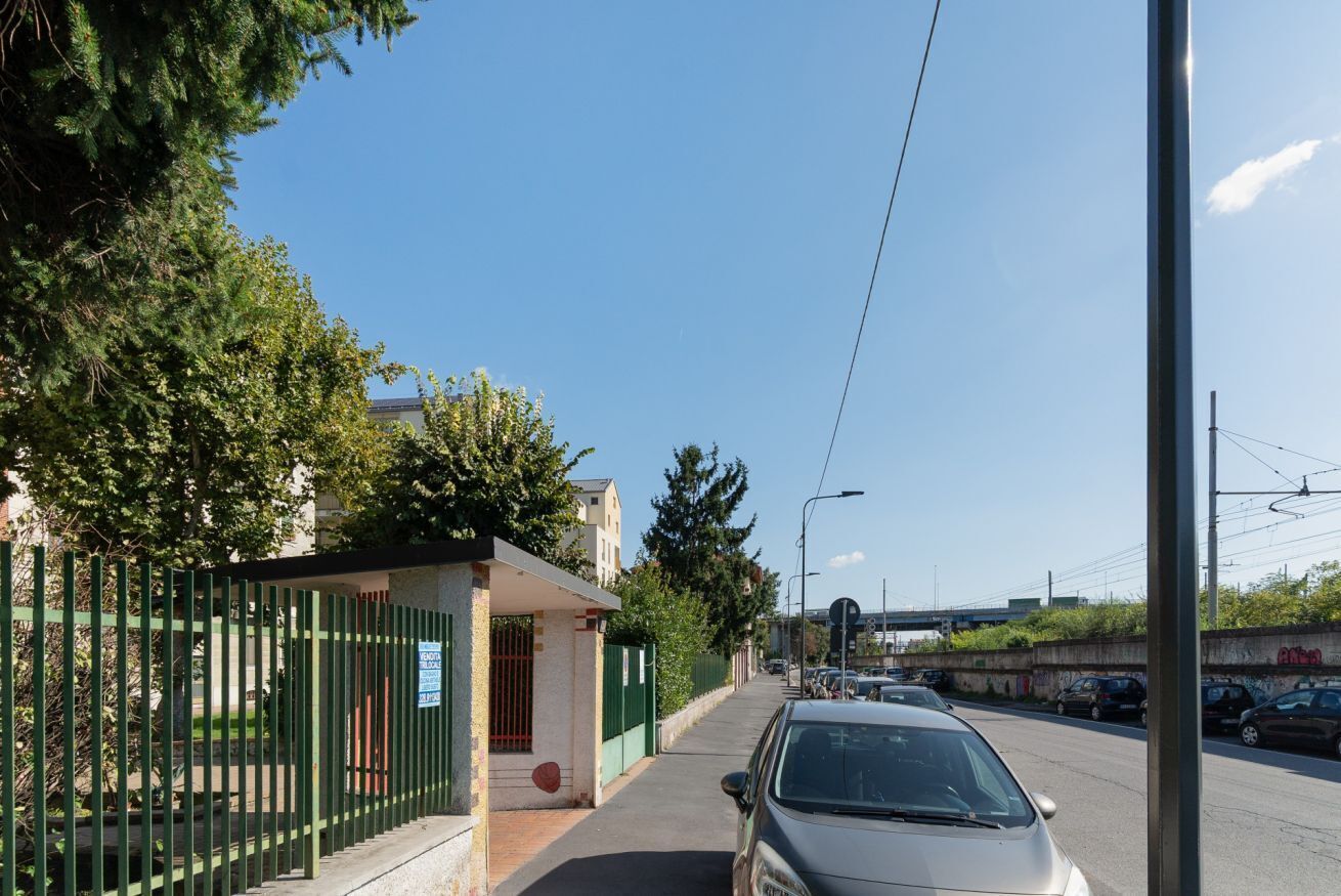A street with a building, a green fence, and parked cars.