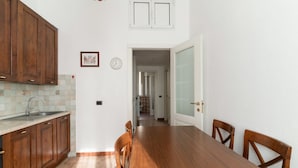 A kitchen with wooden cabinets, a tiled backsplash, a dining table with chairs, and a hallway leading to another room.