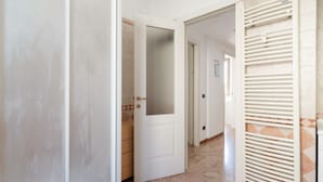 A hallway with a white door, a radiator, and a tiled floor.