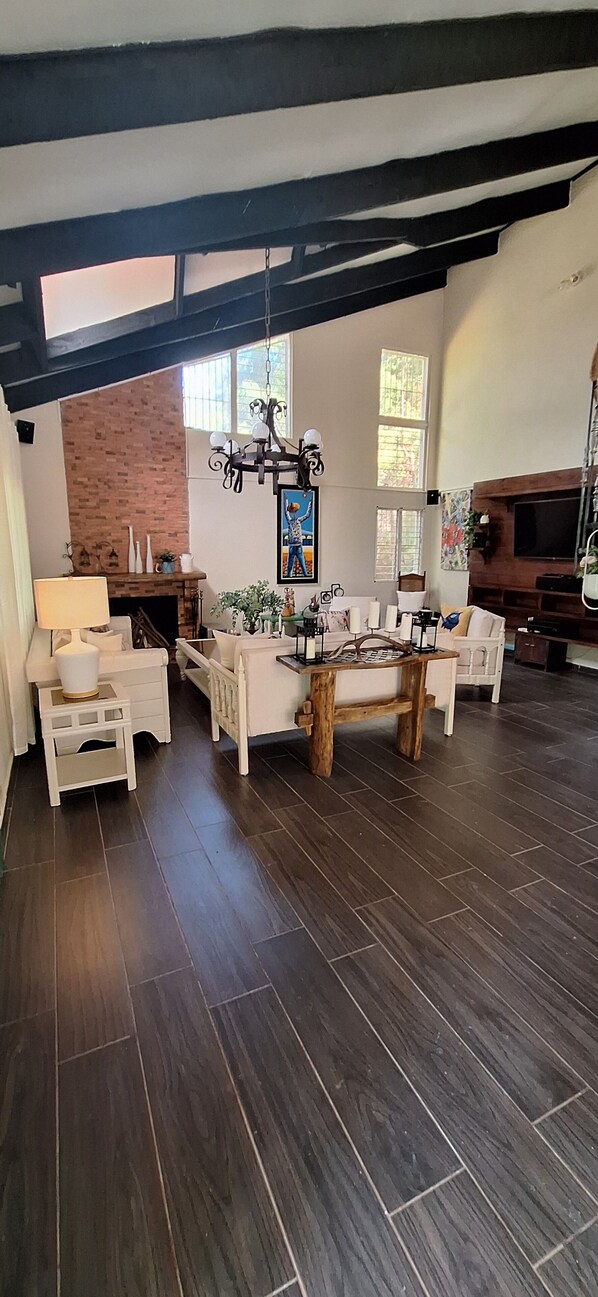 Un salon spacieux doté d’un parquet en bois foncé, d’une cheminée, d’un lustre et d’un téléviseur.