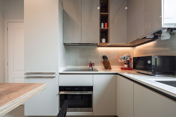 A modern kitchen with white cabinetry, a stainless steel oven, a microwave, and a wooden table.