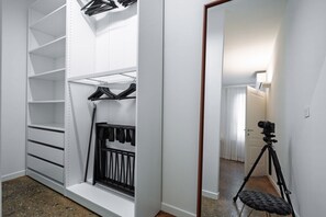 Un vestidor con repisas abiertas, una barra para colgar ropa y una cámara sobre un trípode en la habitación contigua.