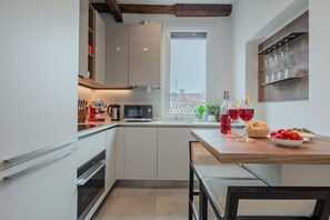 A compact kitchen with a window, a dining table with chairs, and a wine glass set.
