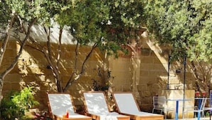 A swimming pool with lounge chairs and a table, surrounded by stone walls and greenery. - Alba (Sliema)