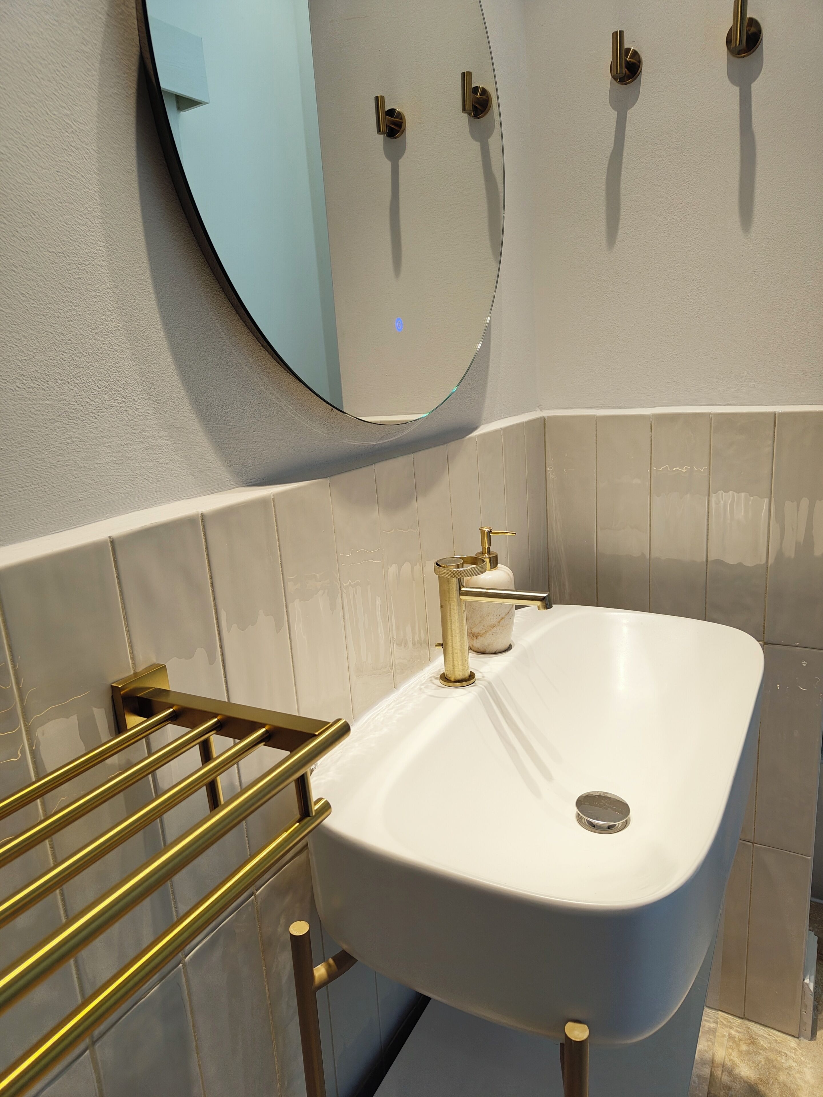 A bathroom with a white sink, gold fixtures, and a round mirror.