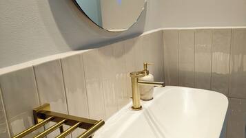 A bathroom with a white sink, gold fixtures, and a round mirror.