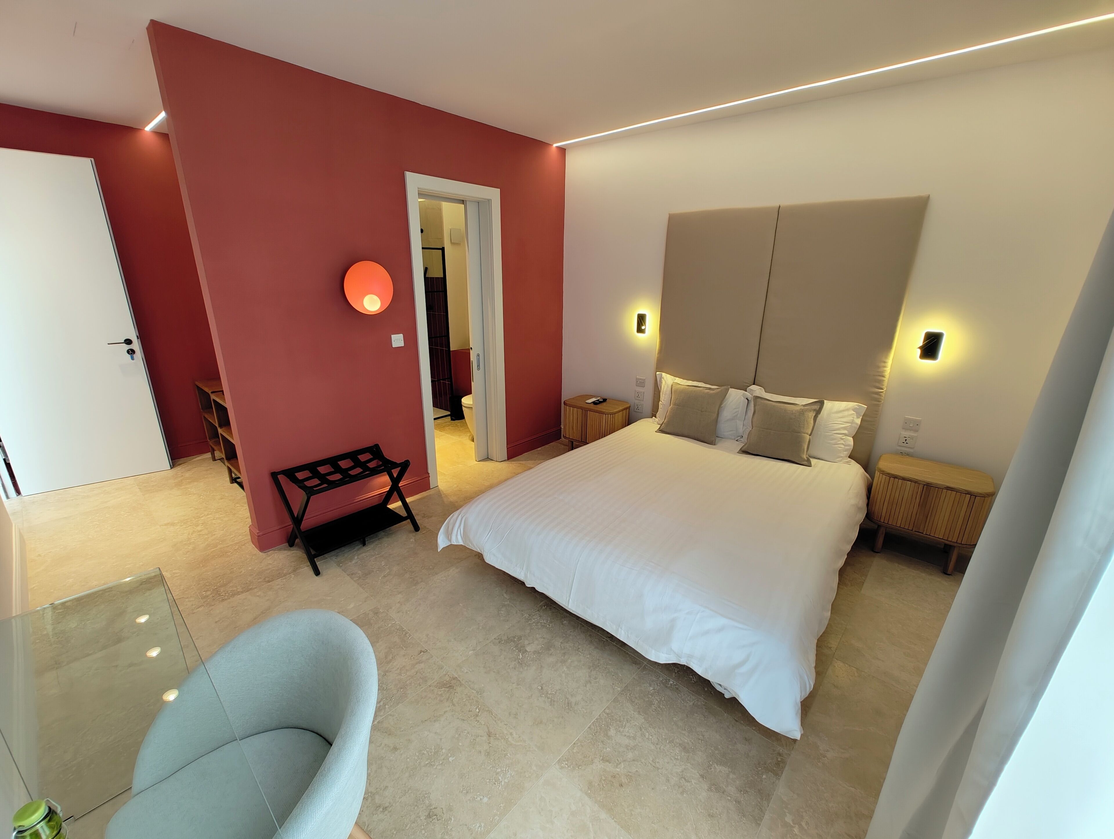 Une chambre d’hôtel moderne dotée d’un grand lit, d’un coin salon avec un banc et d’une cloison en verre.
