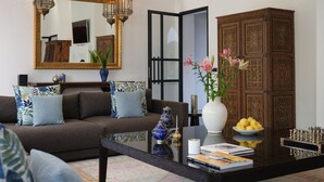 A living room with a brown sofa, patterned cushions, a glass coffee table, a white vase with flowers, a decorative cabinet, and a chess set. - YALI, private house in the heart of the Four Seasons Resort Marrakech (Marrakech)