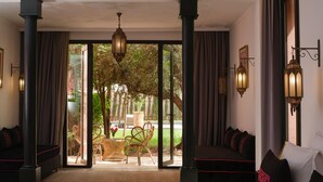 A hotel room with a large bed, two seating areas, and a view of a garden through glass doors. - YALI, private house in the heart of the Four Seasons Resort Marrakech (Marrakech)