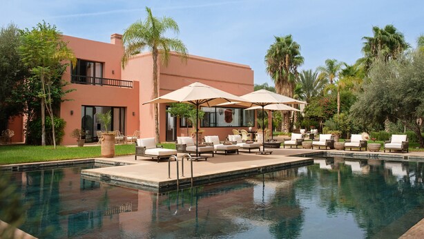 A poolside area with lounge chairs and umbrellas, a modern building with large windows, and a clear blue sky. - YALI, private house in the heart of the Four Seasons Resort Marrakech (Marrakech)