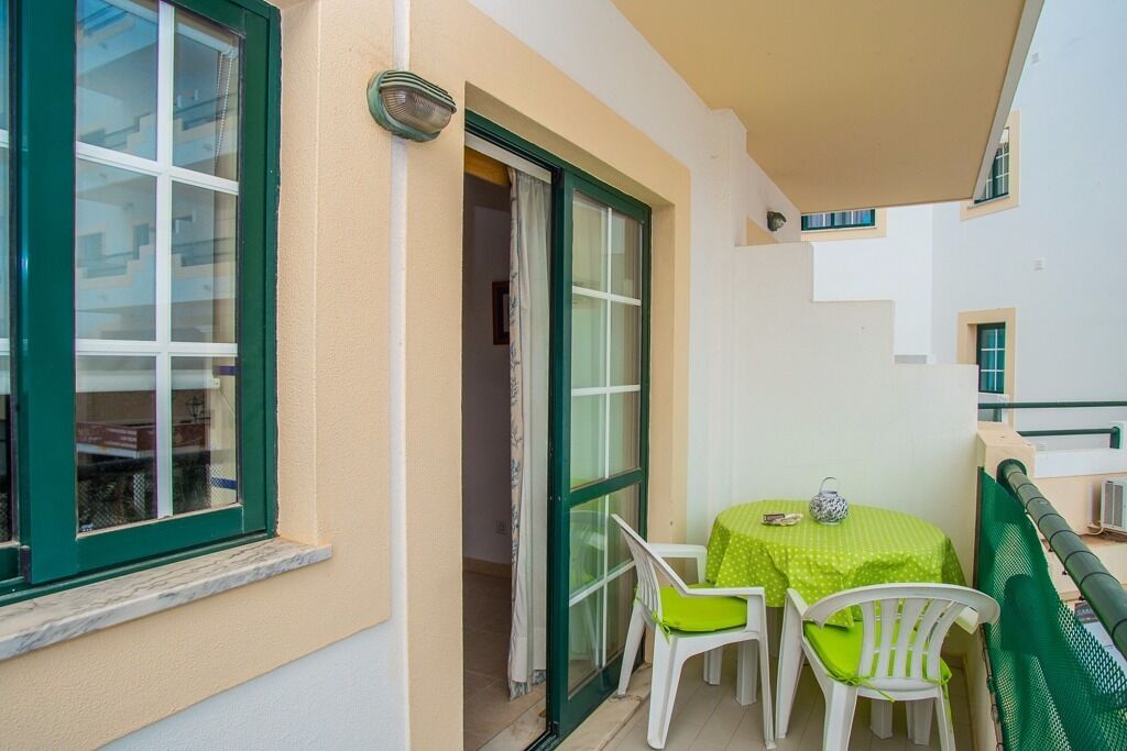 Varanda com mesa, cadeiras, porta de correr de vidro e guarda-corrimão verde.