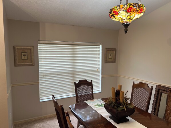 Un coin repas avec une table en bois, des chaises, un luminaire en vitrail et deux tableaux encadrés accrochés au mur.